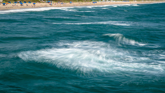 Deep aqua waters rolling into beach with many sunbathers