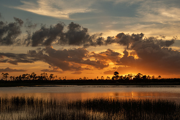 Sun below horizon withbrilliant orange skies, dark clouds and water reflections